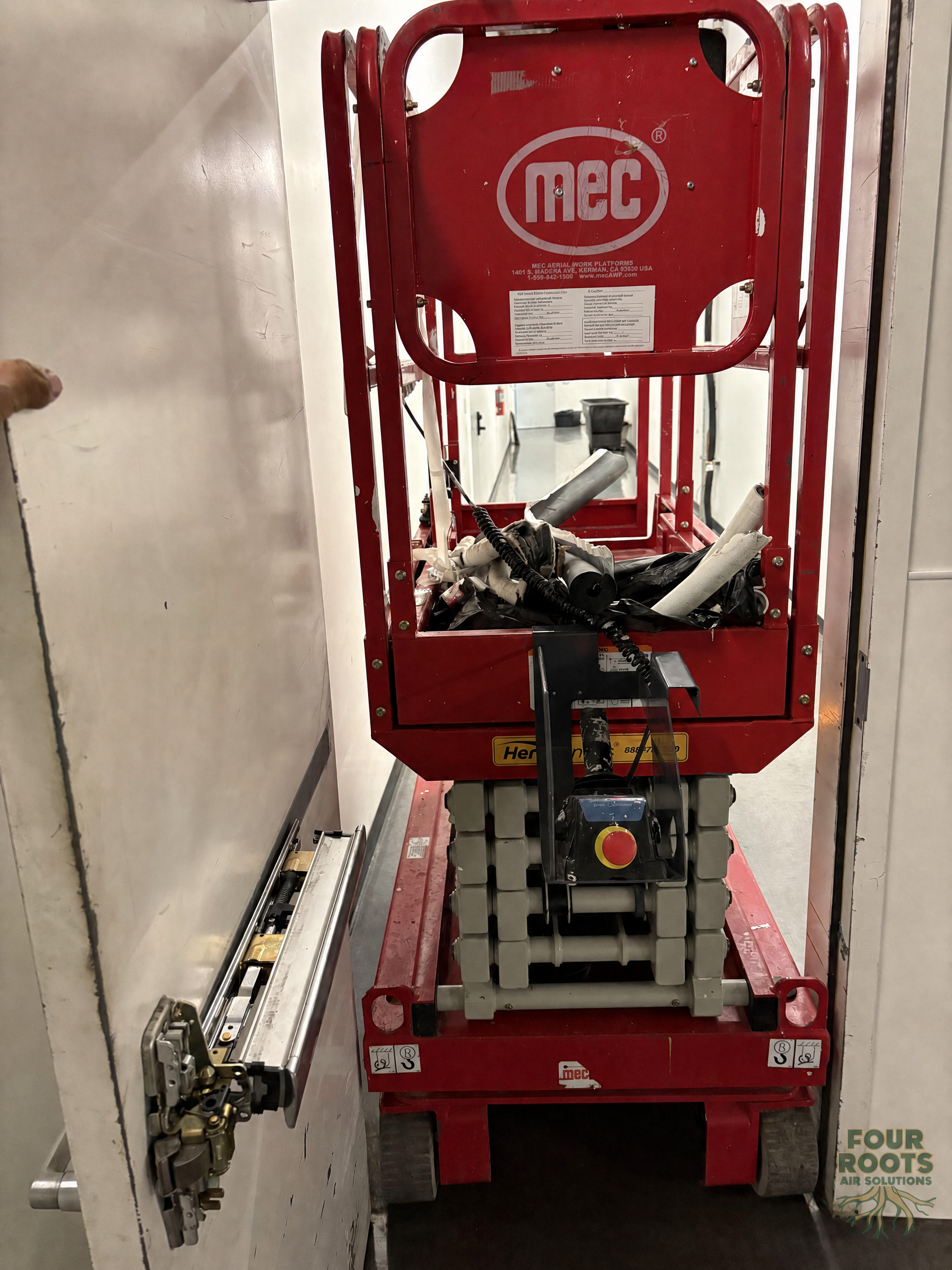 Red scissor lift positioned with very narrow clearance through a restaurant service doorway.