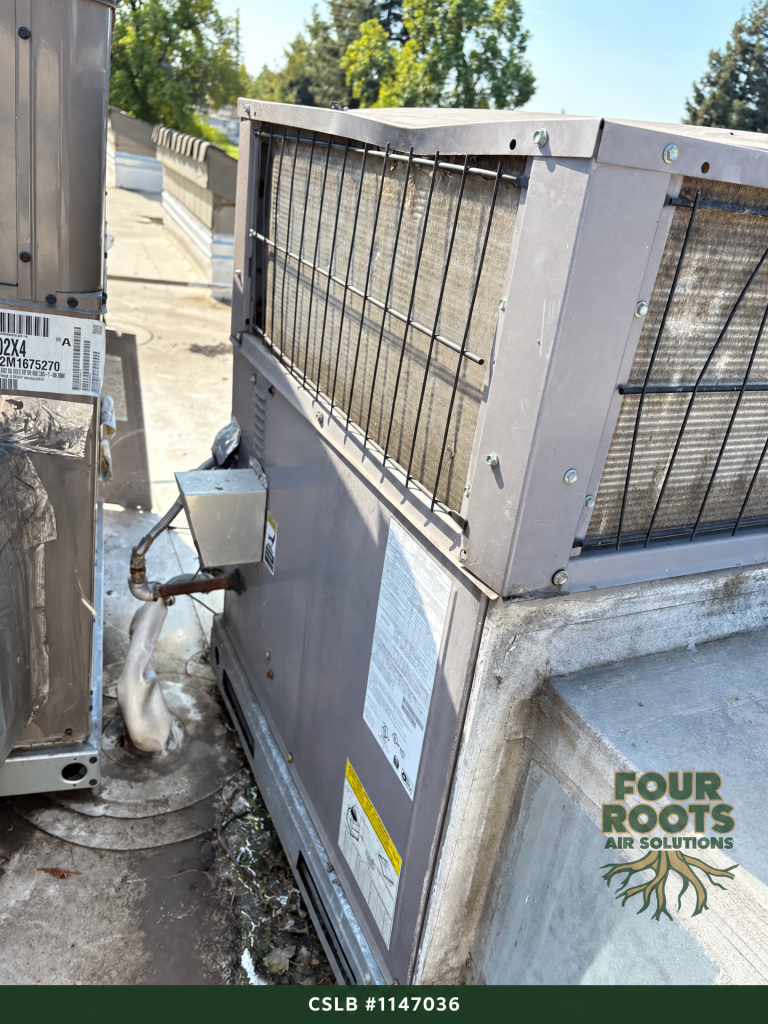 Rooftop HVAC package unit with dirty coil behind a wire guard, sitting close to a neighboring unit on an apartment roof.