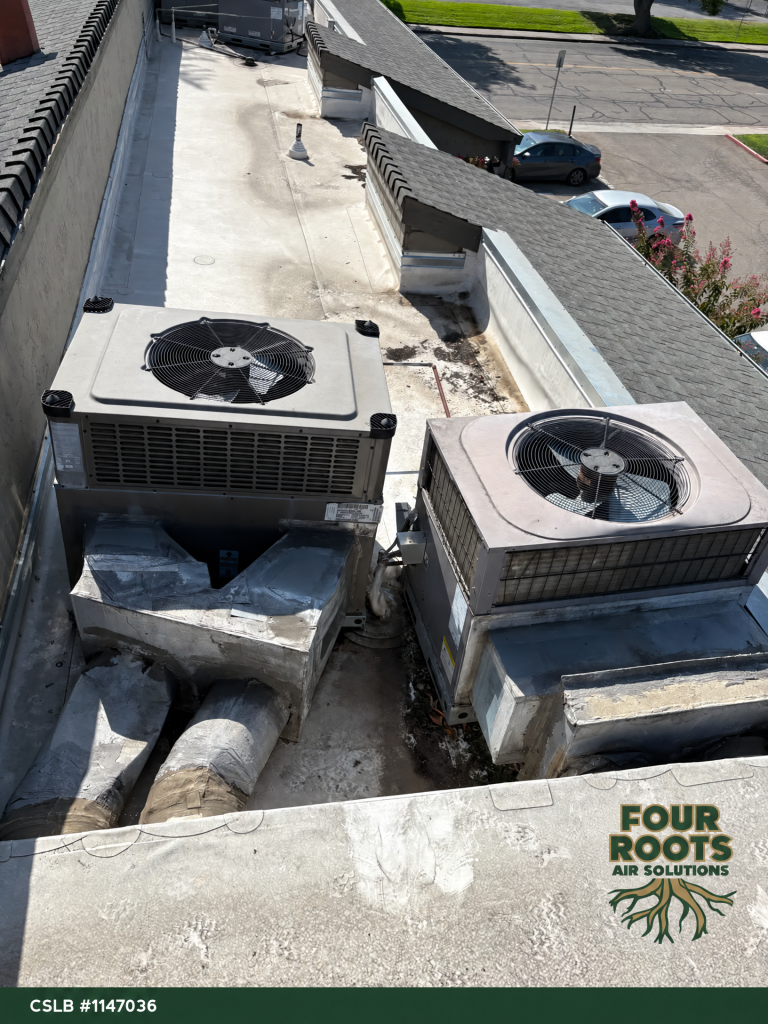 Overhead view of two rooftop HVAC units placed close together on a flat apartment roof, with taped insulated ductwork.