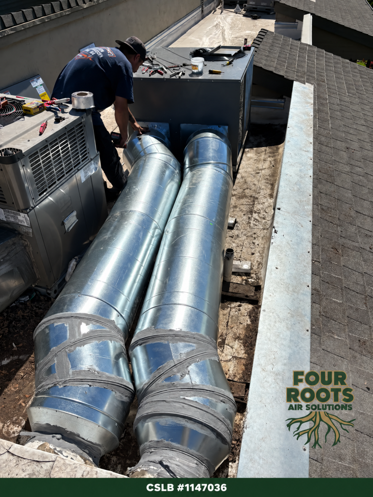 HVAC technician connecting two new galvanized metal-jacketed supply and return ducts to a rooftop unit.